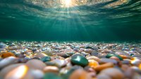 Underwater sunbeams pierce through crystal clear water illuminating colorful smooth pebbles and stones on seabed, creating magical aquatic atmosphere.