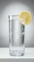 Glass of sparkling water with ice and fresh lemon slice garnish on white surface, refreshing beverage for advertising, packaging, and culinary design projects.