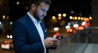 Professional businessman using smartphone at night in urban city with bokeh lights background for mobile technology and communication concepts.