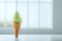 Mint green ice cream scoop in crispy waffle cone standing upright on white surface against bright window background, minimal summer dessert composition.