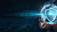 Digital cybersecurity shield hologram floating above hand with glowing circuit board patterns and network connections on dark blue technology background.