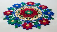 Colorful traditional folk embroidery with floral mandala pattern on white fabric featuring red blue green flowers and decorative stitching for textile design.
