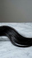 Long dark hair strand flowing on white marble surface with gray wall background for beauty and haircare concepts.