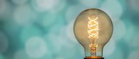 Vintage Edison light bulb with glowing filament against soft turquoise bokeh background for creative inspiration and innovation concepts in modern interior design.