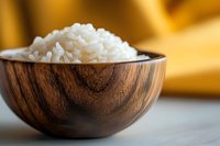 Cooked white rice in wooden bowl on marble surface with warm golden background, suitable for food photography, culinary blogs, and restaurant menus.