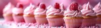 Fresh raspberry cupcakes with pink cream frosting arranged in row, topped with whole berries against pink background, selective focus on dessert.