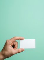 Hand holding blank white business card against turquoise background, ready for custom branding and contact information design.