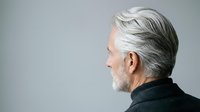 Senior man with white hair and beard in profile view against neutral background, wearing dark clothing for portrait and healthcare concepts.