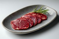 Fresh raw beef tenderloin steaks sliced on gray ceramic plate with rosemary sprig, marbled meat texture on neutral background for food photography.