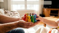 Diverse wooden rainbow people figures held in cupped hands symbolizing unity, inclusion, community support and teamwork in warm home setting.