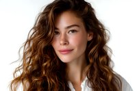 Young Asian woman with flowing brown wavy hair and natural makeup smiling confidently against white background, wearing casual white shirt. Professional portrait.
