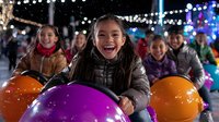 Young Asian girl laughing with pure joy at winter festival, surrounded by colorful illuminated spheres and friends, capturing authentic happiness in evening celebration.