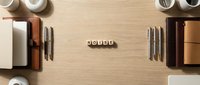 Professional workspace flat lay with leather notebooks, pens, coffee cups and wooden letter blocks spelling HOUSE on natural wood background for real estate branding.