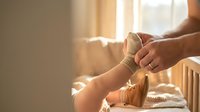 Person putting on beige ankle support brace in bright bedroom setting for injury recovery and foot care rehabilitation.