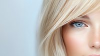 Close up portrait of young woman with platinum blonde hair and bright blue eyes against light background, soft focus beauty shot highlighting natural makeup.