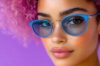 Close up portrait of young mixed race woman wearing bright blue cat eye glasses against purple background, showing full lips and confident expression.