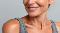 Close-up portrait of smiling mature Caucasian woman with healthy skin wearing gray tank top against neutral background.