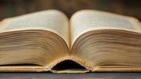 Open hardcover book with pages spread wide, revealing layered paper texture and natural lighting. Shallow depth of field creates dreamy atmosphere for education concepts.