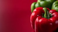 Fresh red and green bell peppers with water droplets on vibrant red background for healthy cooking and nutrition concepts.