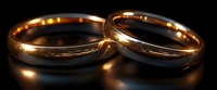 Two golden wedding rings on dark reflective surface with soft lighting and romantic glow, symbolizing marriage, commitment and eternal love.
