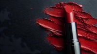 Red lipstick with smeared creamy texture on dark background, dramatic cosmetic product photography showing rich pigment and smooth consistency.