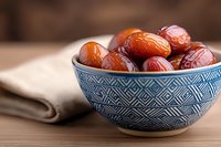 Fresh organic dates in traditional blue ceramic bowl with geometric pattern on wooden table, healthy dried fruit snack for natural sweetness.