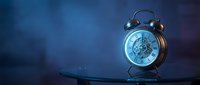 Vintage brass alarm clock with visible gears on glass surface, glowing blue light, dark moody background, copy space for text.
