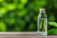 Clear plastic bottle with pure water on wooden surface against blurred green natural background, fresh spring leaves reflected in glass container.