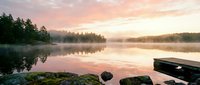 Serene lake at sunrise with misty forest reflection, calm water, and rocky shoreline creating peaceful nature landscape for relaxation and wellness.