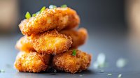 Crispy golden chicken nuggets stacked with fresh herbs garnish on dark background, selective focus capturing steam and texture of breaded coating.