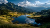 Serene mountain landscape with blue lake reflecting clouds and sky, surrounded by lush green hills and distant peaks in golden afternoon light.
