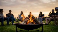 Friends gathering around outdoor fire pit during golden hour sunset creating warm social atmosphere for camping and backyard entertainment activities.
