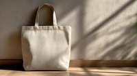 Blank canvas tote bag against neutral wall with soft shadow play, perfect for eco-friendly shopping, branding mockups, or sustainable lifestyle concepts.