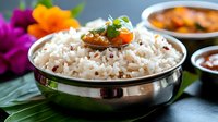Steamed white rice garnished with fresh herbs and cherry tomato served in traditional metal bowl with curry sauce and condiments on banana leaf background.