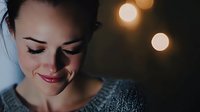 Young woman with closed eyes and gentle smile enjoying peaceful moment in warm ambient lighting with soft bokeh background.