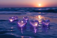 Glowing pink heart-shaped crystals on wet beach sand at sunset with ocean waves and purple twilight sky creating romantic atmosphere for love concepts.