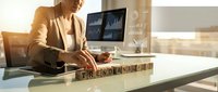 Businesswoman arranging wooden blocks spelling trend analysis at office desk with financial charts on monitor in background.
