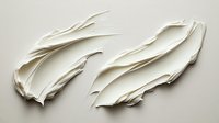 White cream cosmetic texture smear on light background, smooth wavy strokes showing skincare product consistency and luxurious moisturizer application technique.