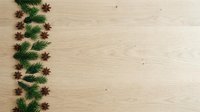 Evergreen branches and star anise arranged in decorative border on light wooden surface, suitable for holiday greeting cards, seasonal marketing materials, and festive design projects.