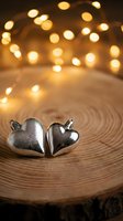 Two silver heart-shaped Christmas ornaments on wooden surface with warm bokeh lights creating festive holiday atmosphere for seasonal decorations.