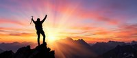 Silhouette of triumphant hiker with raised arms celebrating success on mountain peak at sunrise with dramatic colorful sky and mountain ranges below.