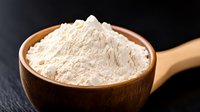 White flour in wooden bowl and spoon against dark background, macro food photography with selective focus on organic baking ingredient.