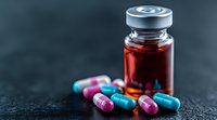 Medical capsules in pink and blue colors scattered near brown glass vial on dark background. Pharmaceutical and healthcare concept for drug prescriptions.