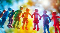 Colorful paper cutout children silhouettes holding hands in rainbow order against bright bokeh background, representing unity, childhood and diversity in education.