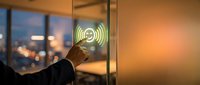 Young adult male hand touching illuminated wireless signal icon on glass door at dusk, representing smart building technology and connectivity solutions for modern offices.