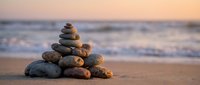 Balanced stone cairn on sandy beach at sunset with soft ocean waves in background creating peaceful zen meditation atmosphere for wellness and mindfulness concepts.