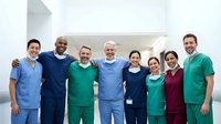 Diverse medical team of doctors and nurses in scrubs posing together in hospital corridor, representing healthcare teamwork and professional collaboration.