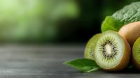 Fresh kiwi fruit sliced in half showing seeds and pulp with green leaves on wooden surface against blurred natural background for healthy eating concepts.