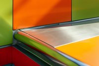 Abstract geometric composition with vibrant orange, yellow, green and red panels intersecting at sharp angles, creating modern minimalist architectural detail.