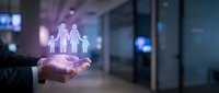 Businessman hand holding glowing family protection icon in modern office environment representing insurance coverage and financial security services.